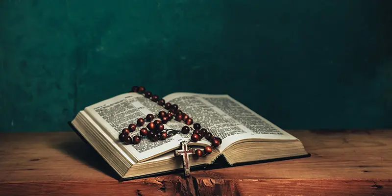 A rosary draped over the open pages of a Bible, symbolizing the Scripture study that forms the heart of pilgrimage preparation