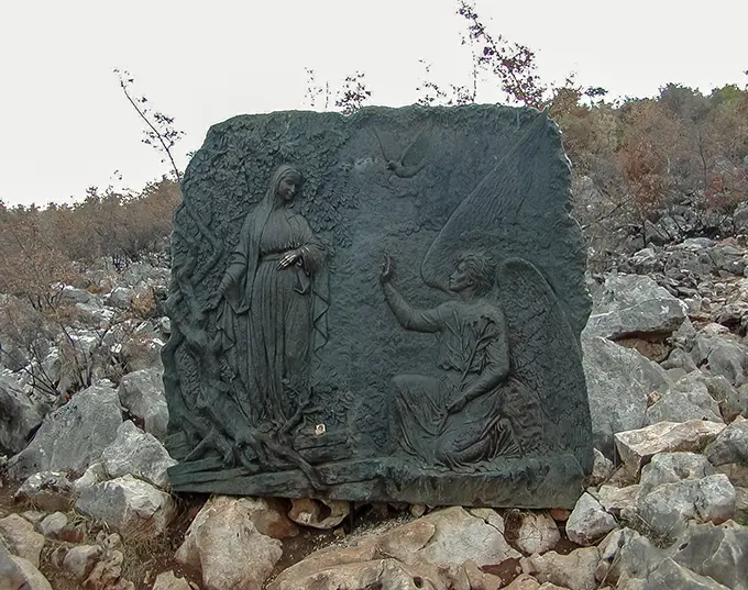 The path rises through bronze reliefs depicting the mysteries of the rosary — most pilgrims pray a decade at each.