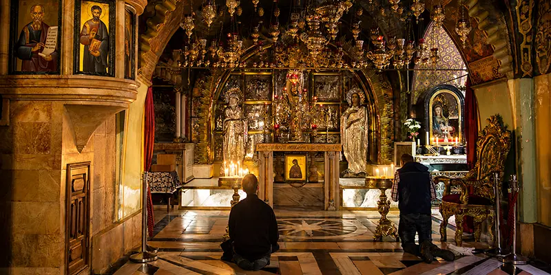 Pilgrims gathered inside the Church of the Holy Sepulchre in Jerusalem, candles in hand near the Aedicule enclosing Christ's tomb