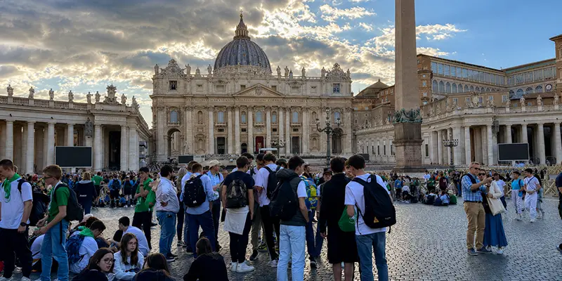 Pilgrims gathered in conversation outside a basilica; the quiet hour between sites is often where pastoral care happens.