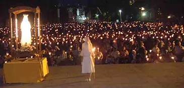 The statue of Our Lady of Lourdes and a religious sister at the head of the nightly Marian Torchlight Procession, thousands of pilgrim candles filling the Esplanade beyond, France