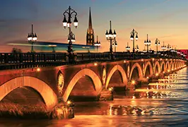 The Pont de Pierre stone bridge over the Garonne River in Bordeaux, France, with the Basilica of Saint Michael rising behind it
