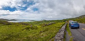 A coastal water view along the Ring of Kerry, with a car on the winding road