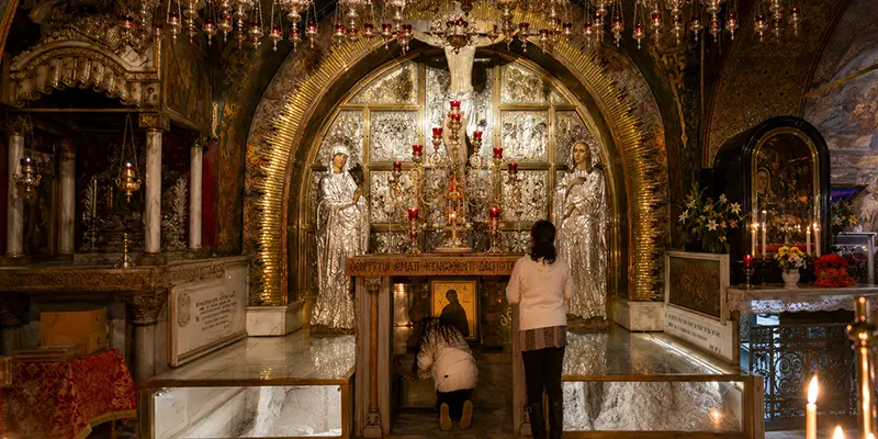 The Rock of Calvary beneath the Greek Orthodox altar, pilgrims kneeling to touch the stone through the opening under the altar.