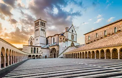 Basilica of St. Francis of Assisi and its colonnaded lower plaza at sunset — Italy pilgrimage