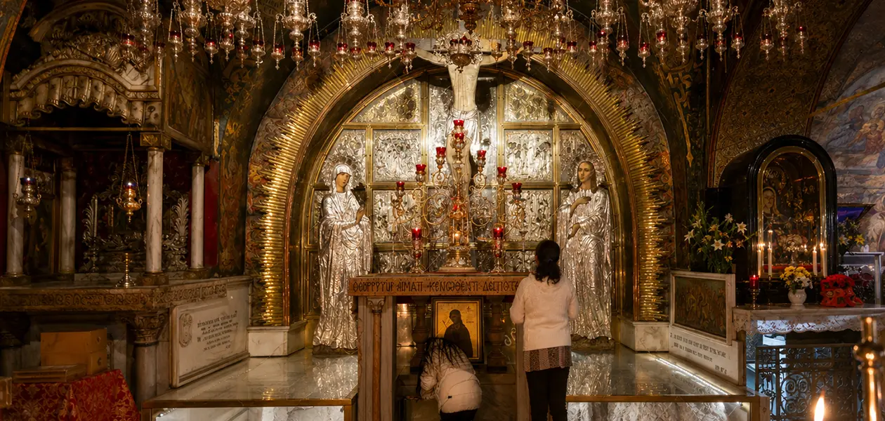Pilgrims at the Rock of Calvary on Golgotha inside the Church of the Holy Sepulchre in Jerusalem, beneath hanging lamps and the mosaics of the Chapel of the Crucifixion