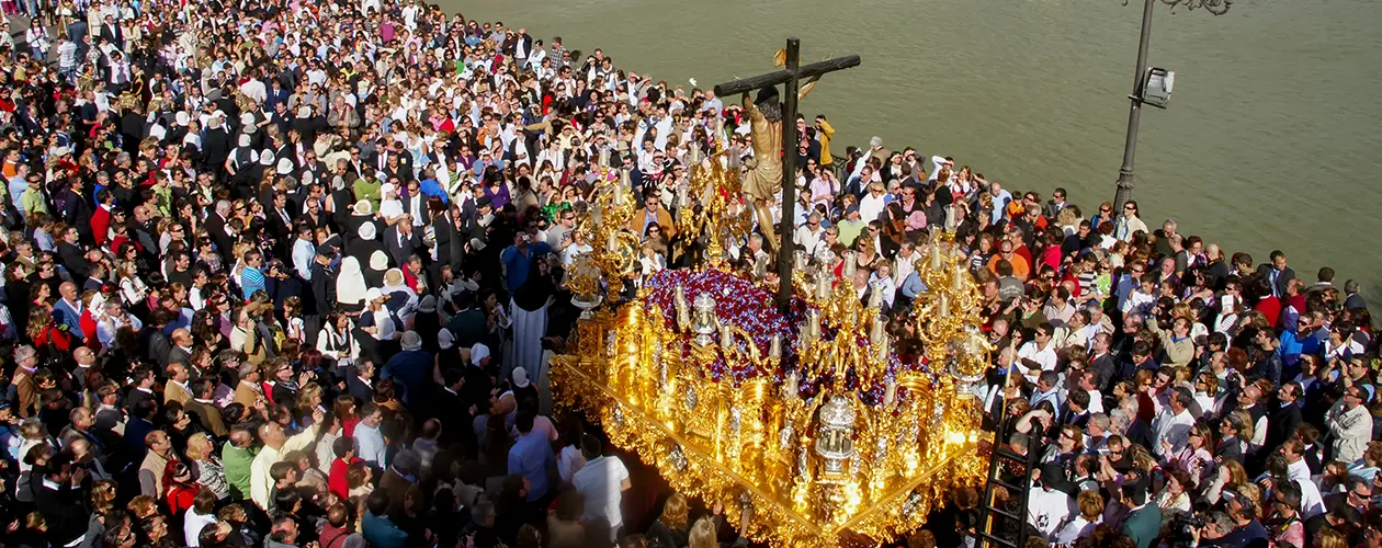 Semana Santa procession in Seville, Spain: a gilded float bearing Christ on the cross is carried through a crowd along the Guadalquivir River during Holy Week